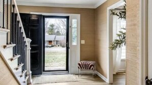 Un pasillo con piso de madera, una puerta negra y una escalera con barandas blancas.