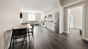 Una cocina moderna con armarios blancos, un refrigerador de acero inoxidable y una zona de comedor con una mesa y sillas de madera.