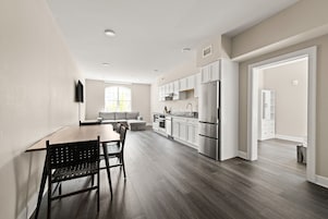 Una cocina moderna con armarios blancos, un refrigerador de acero inoxidable y una zona de comedor con una mesa y sillas de madera.