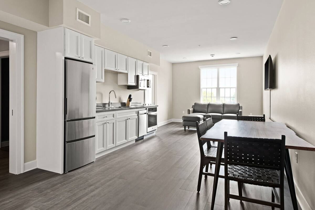 A modern kitchen with white cabinets, stainless steel appliances, and a dining area with a wooden table and chairs.
