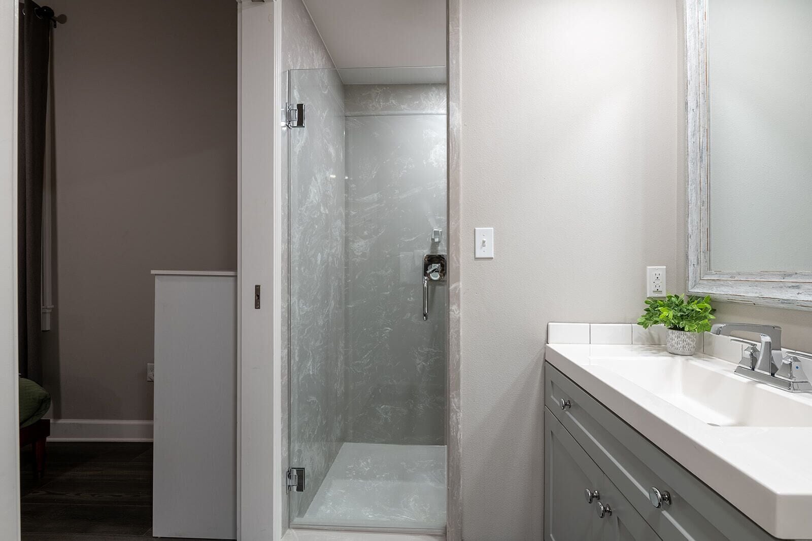 Un baño moderno con ducha envuelta en vidrio, un lavabo blanco con una planta y un espejo grande.
