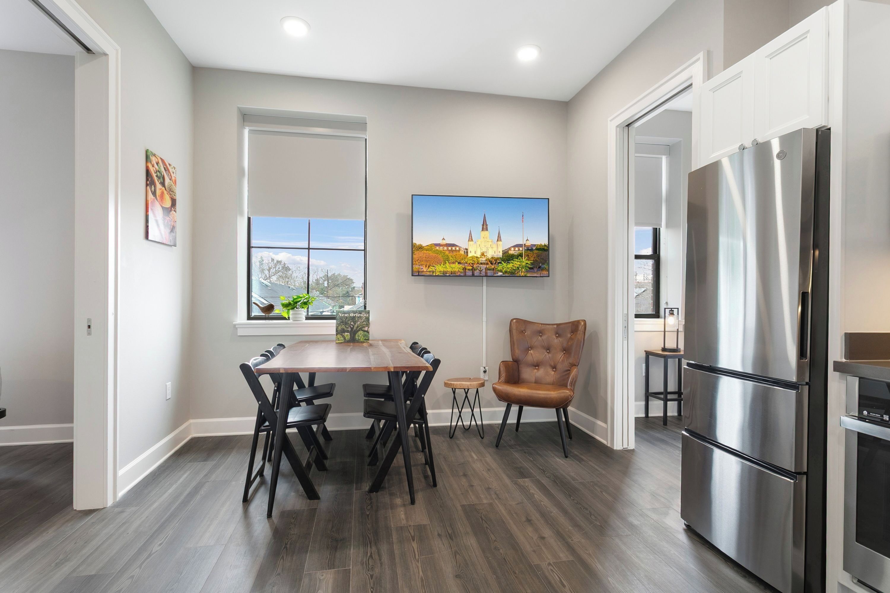 A modern kitchen with a dining table, chairs, a large refrigerator, and a window with a cityscape view.