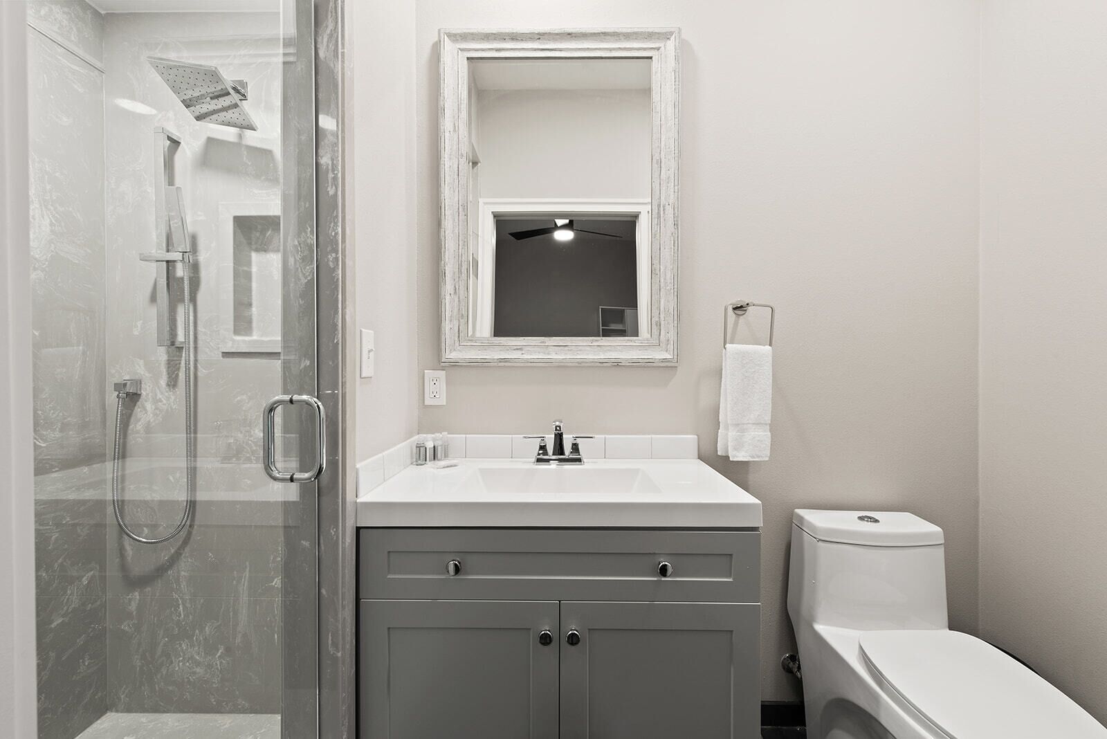 Un baño con ducha de vidrio, lavamanos blanco, espejo y retrete.