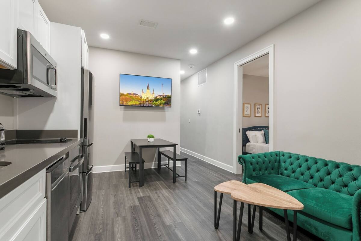 A modern kitchen with stainless steel appliances, a dining area with a table and chairs, and a green sofa in a living space.