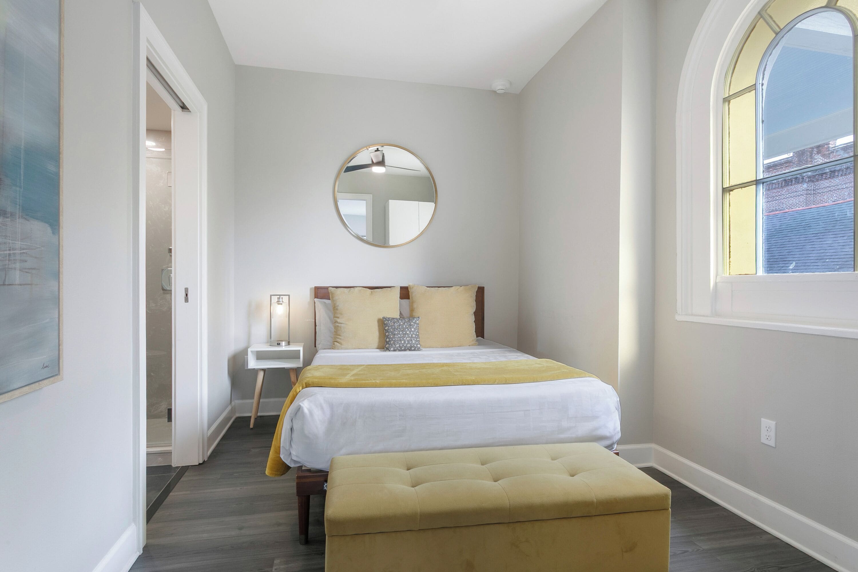 A bedroom with a bed, bedside table, and a round mirror on the wall.