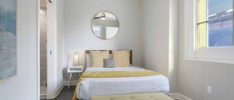 A bedroom with a bed, bedside table, and a round mirror on the wall.