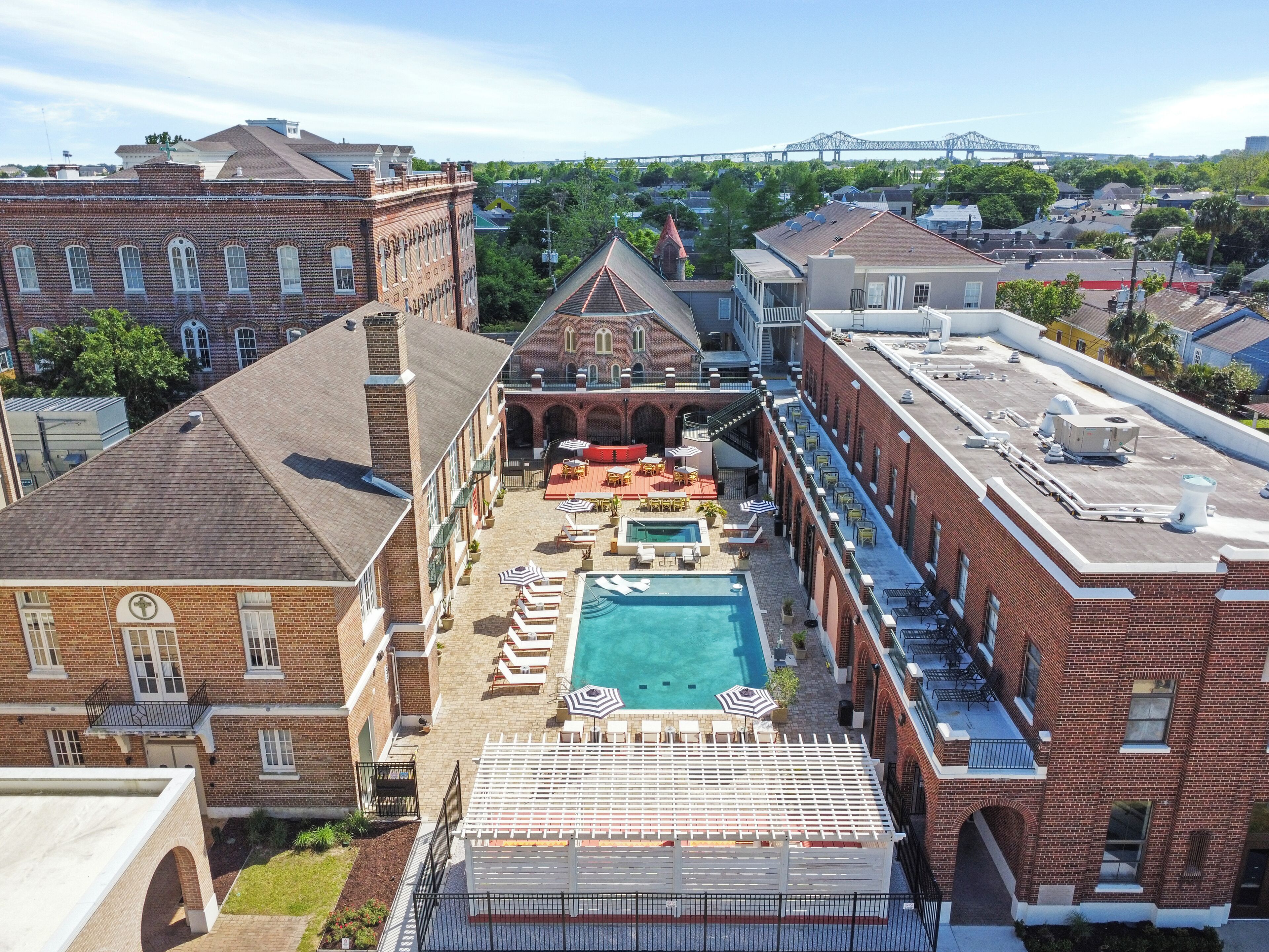 A rooftop pool area with lounge chairs and umbrellas, surrounded by brick buildings with arched windows.