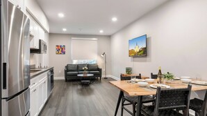 Una cocina moderna con electrodomésticos de acero inoxidable, un comedor con mesa de madera y sillas negras, y un sofá de cuero negro en la sala de estar.