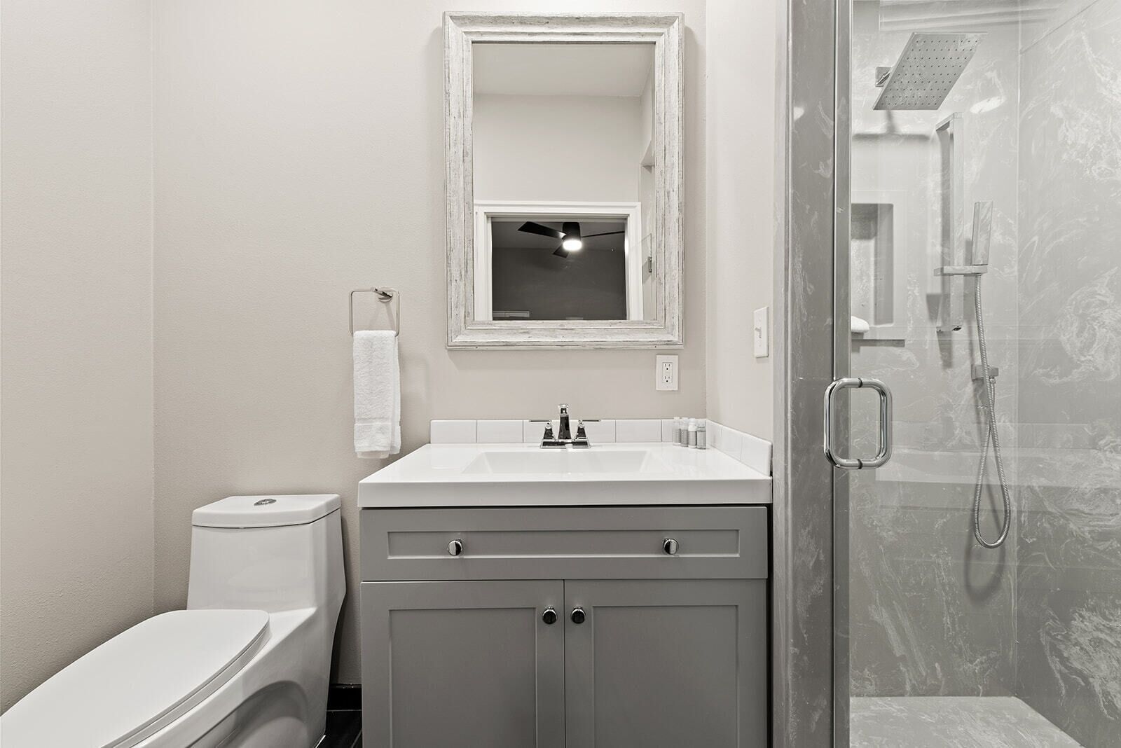 A bathroom with a toilet, sink, mirror, and shower.