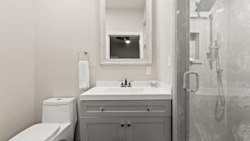 A bathroom with a toilet, sink, mirror, and shower.