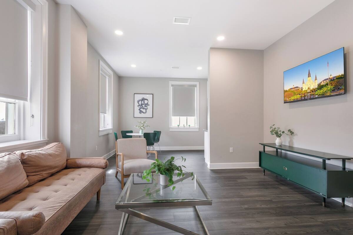 A modern living room with a sofa, a glass coffee table, a dining area with chairs, and a green console table.