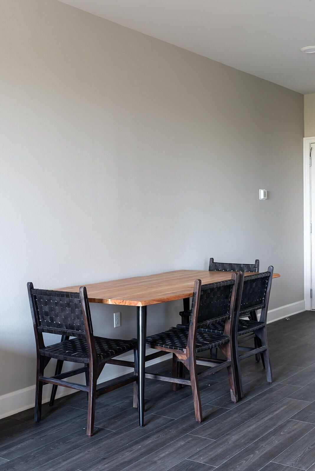 A dining area with a wooden table and two chairs, a light-colored wall, and a dark wooden floor.