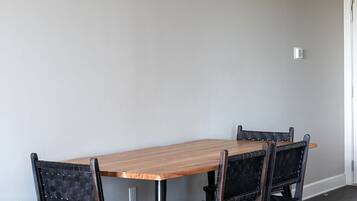 A dining area with a wooden table and two chairs, a light-colored wall, and a dark wooden floor.