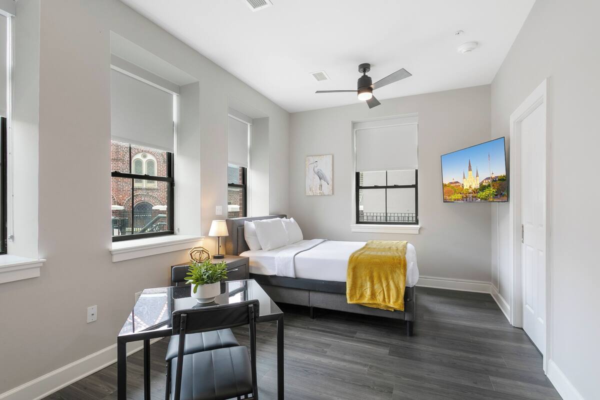 A bedroom with a bed, a desk, a chair, a window, and a ceiling fan.