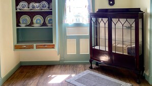 Una habitación con piso de madera, un aparador azul y blanco, un reloj y un mueble de madera oscura con puertas de cristal.