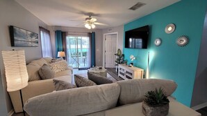 A living room with a sofa, a TV, and decorative wall art. - Refreshed 3BR condo- pool/patio/tennis - 1st Floor (Four Corners)