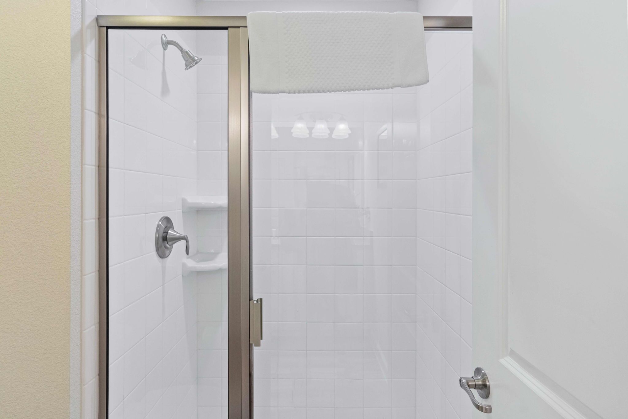 Una ducha con puerta de vidrio, una toalla colgando en la puerta y un secamanos en la pared.