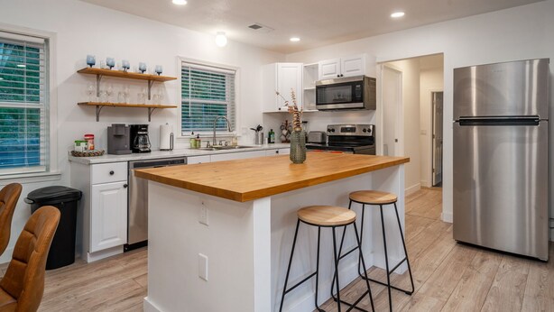 A modern kitchen with white cabinetry, a wooden island, stainless steel appliances, and bar stools.
