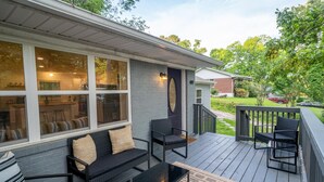 A covered deck with outdoor furniture, a glass door, and a brick exterior.
