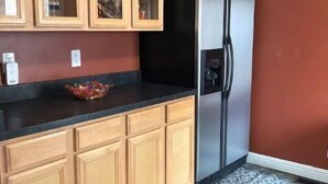 A kitchen with wooden cabinets, a black countertop, a stainless steel refrigerator, and a patterned rug.
