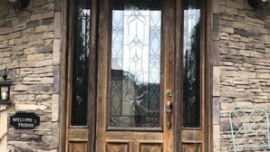 A wooden front door with a glass panel, set in a stone wall, with a welcome sign and a star decoration on the left.