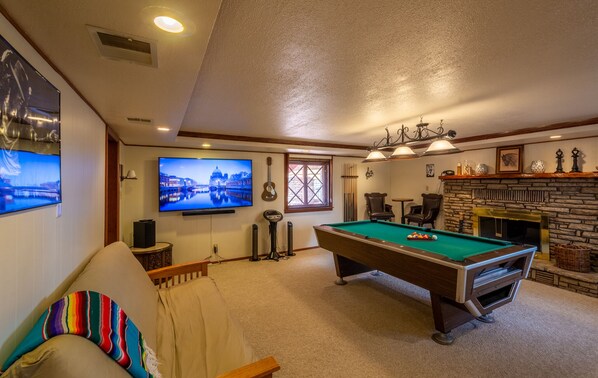 Une salle de jeux avec une table de billard, un téléviseur et une cheminée.