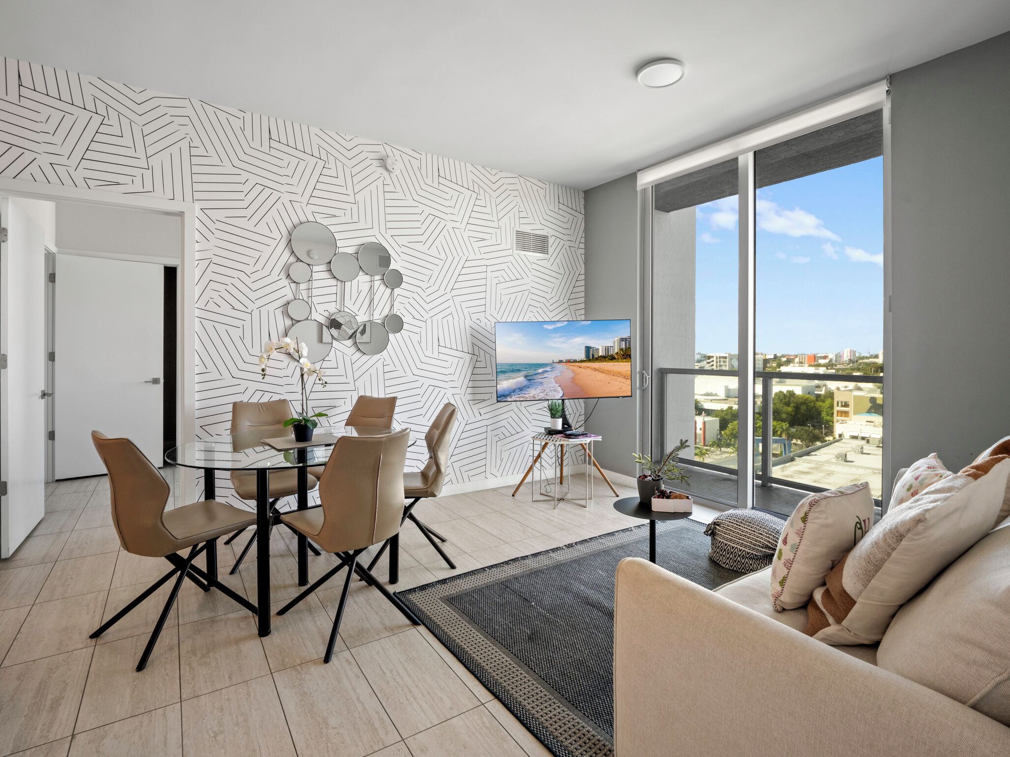 A modern living room with a dining area, large windows, and a city view.
