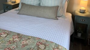 En snyggt bäddad säng med ett blommigt överkast, två sänglampor och en dekorativ väggdekoration ovanför.