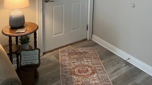 En dörr med ett vitt karm, ett litet bord med en lampa, en matta och en skylt på väggen.