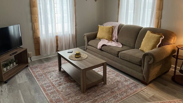 Ett vardagsrum med en soffa, ett soffbord, ett TV-bord och en mönstrad matta.