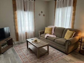 A living room with a sofa, a coffee table, a TV stand, and a patterned rug. - Corporate Cottage in LaPorte Cable St Front unit (La Porte)