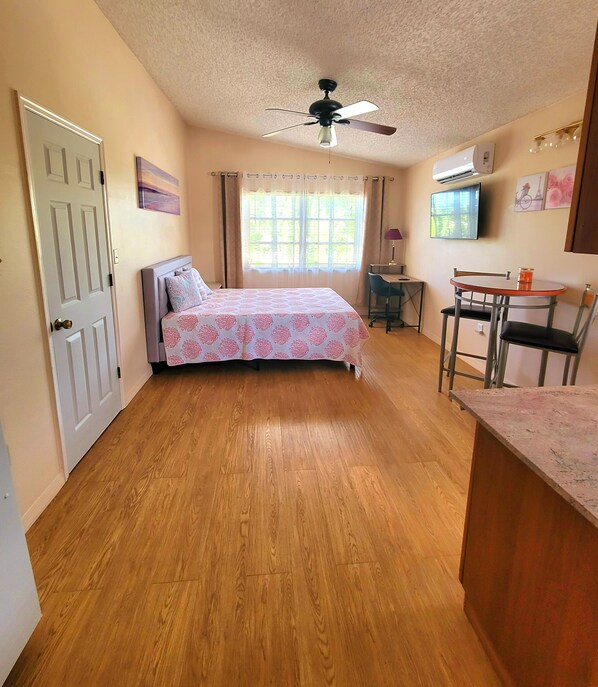 A bedroom with a bed, a desk, a chair, a ceiling fan, and an air conditioning unit.
