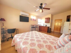 Une chambre comprenant un lit, un bureau, une chaise, un coin cuisine et un ventilateur de plafond.
