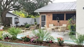 Ein Haus mit einer Terrasse, Gartenmöbeln und einem Garten mit verschiedenen Pflanzen und Blumen.