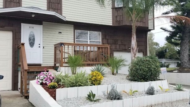 Ein Wohnhaus mit Veranda, Briefkasten und einem gepflegten Garten mit verschiedenen Pflanzen und Blumen.