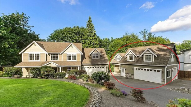 Une maison à deux étages avec un garage, entourée d’une pelouse bien entretenue et d’arbres.
