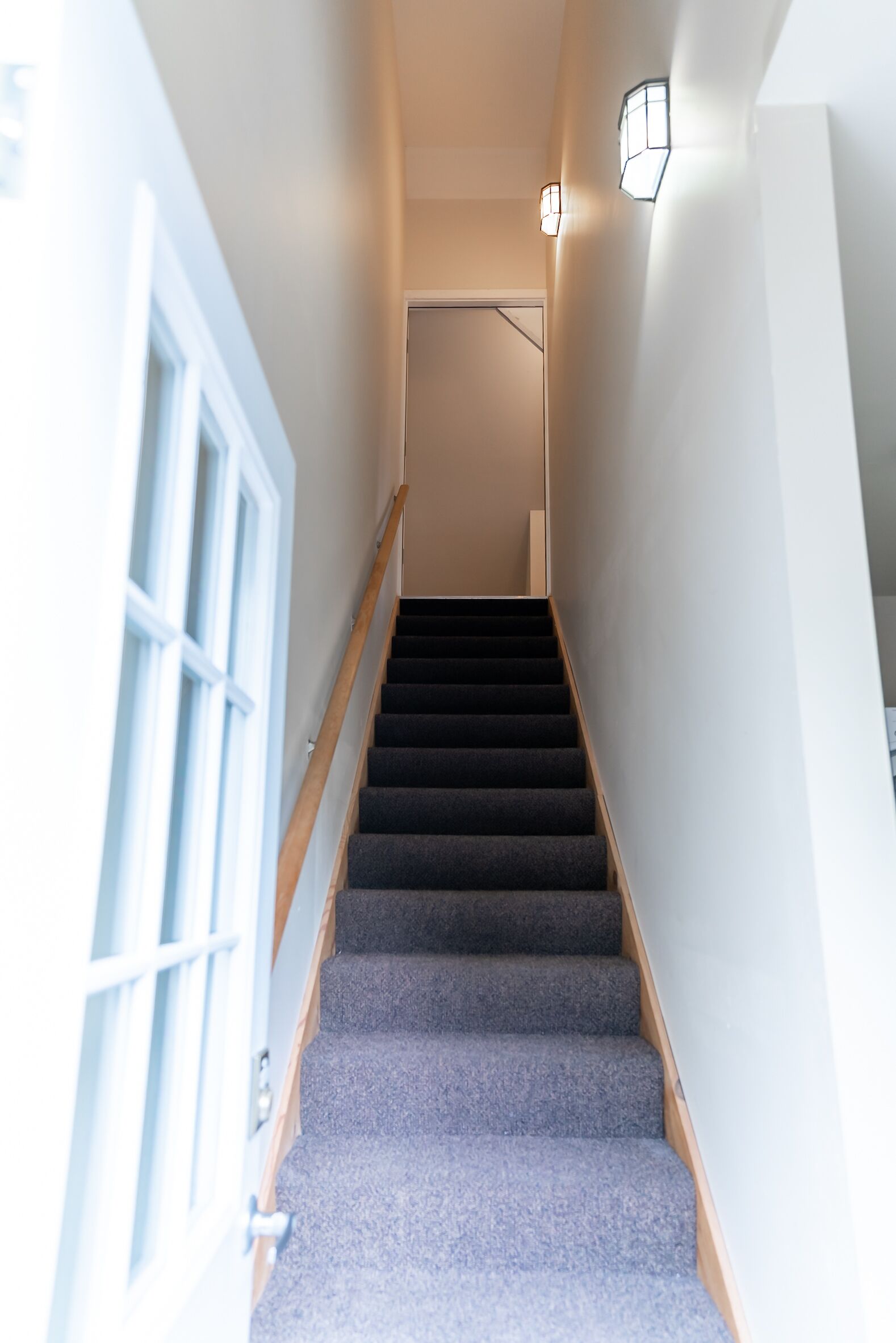 Eine Treppe mit Teppichstufen und Holnänderungen, die zu einer Tür mit einer Leuchte darüber führt.