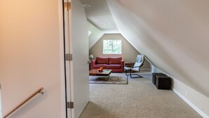 Un loft spacieux avec un plafond haut, un canapé en cuir rouge, une petite table et une fenêtre laissant entrer la lumière naturelle.