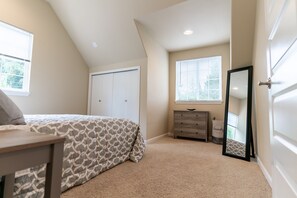 Ein Schlafzimmer mit Bett, Kommode, Spiegel, Fenster und Kleiderschrank.