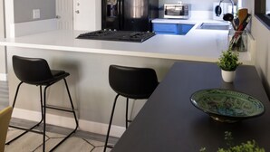 Une cuisine moderne avec un poêle noir, des appareils en acier inoxydable et des armoires bleues. On y trouve deux tabourets de bar noirs et une petite plante en pot sur le comptoir.