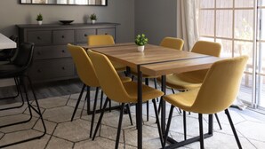 Un coin repas avec une table ronde en bois, six chaises jaunes, un buffet gris et une grande fenêtre avec des rideaux.