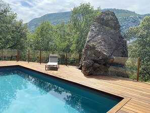 Une piscine avec une terrasse en bois, un fauteuil de relaxation et, au fond, une grande formation rocheuse.