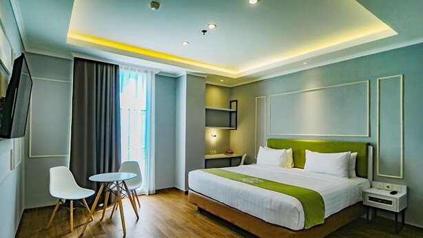A modern hotel room with a large bed, a desk, two chairs, a TV, and a window with curtains. - Hotel Dafam Enkadeli Thamrin Jakarta (Jakarta)