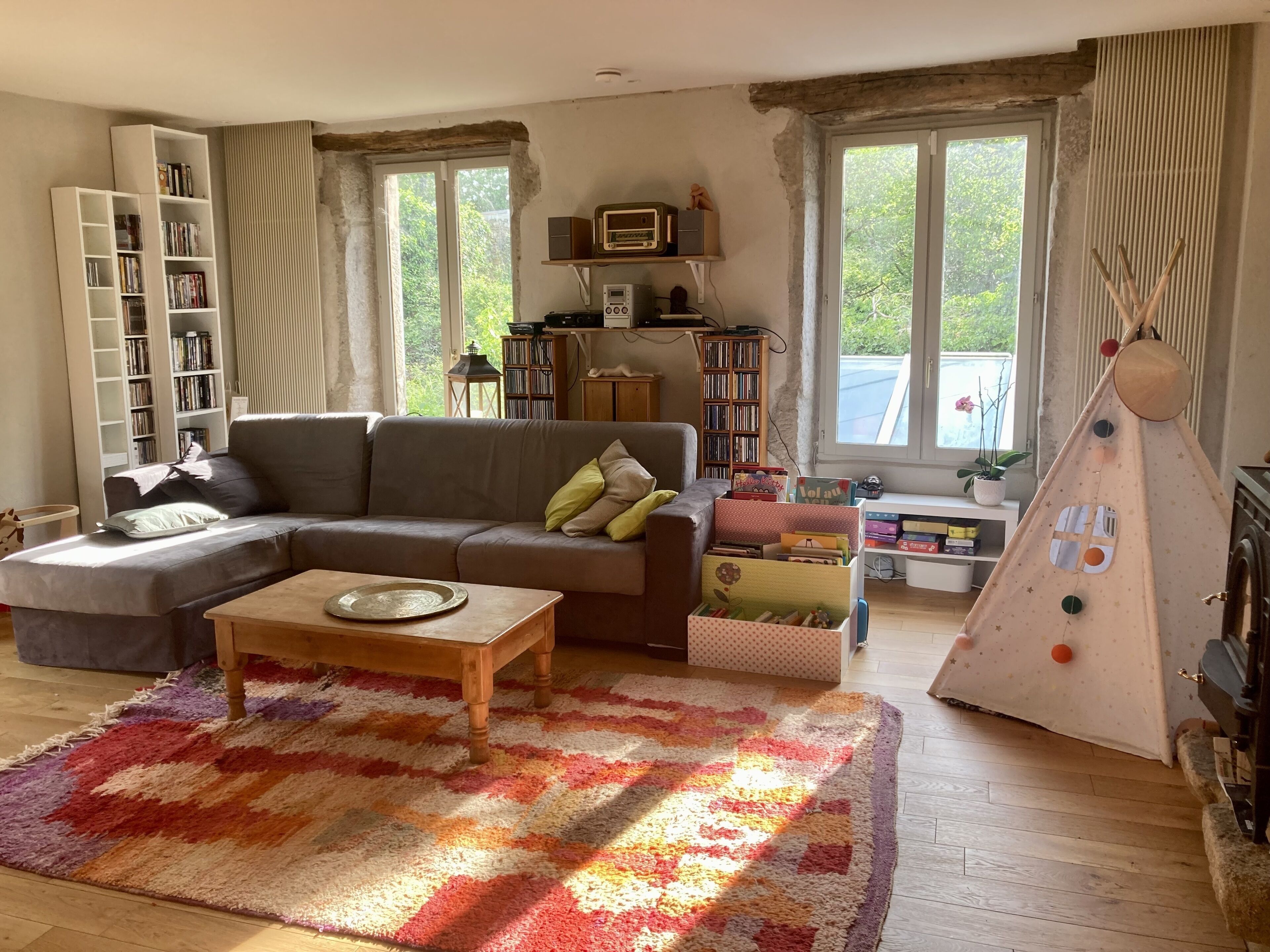 Ein gemütliches Wohnzimmer mit einem Ecksofa, einem Couchtisch, einem Bücherregal, einem Fenster mit Aussicht und einer Teepee-Dekoration.