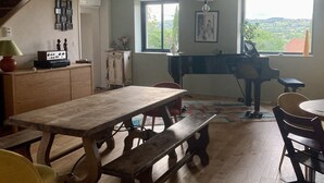 Ruokailutilassa on puinen pöytä ja penkit, piano sekä suuret ikkunat, joista avautuu näkymä maaseudulle.