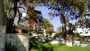 A modern building with a stone facade, a well-maintained garden with various plants, and a clear sky.