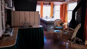 A cozy kitchen with a wooden countertop, a sink, and a table with a green tablecloth. There is a wicker chair and a stone wall in the background. - Cities Of the World - Cusco City Views (Cusco)