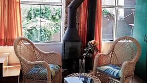 A rustic room with a stone chimney, wicker furniture, and a view of greenery outside. - Cities Of the World - Cusco City Views (Cusco)