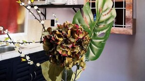 Un coin repas avec une table dressée pour deux personnes, un vase rempli de fleurs et un meuble en bois doté d’étagères.