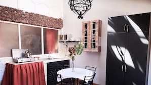 Une cuisine compacte équipée d’une cuisinière à gaz, d’un évier, d’une table à manger avec quatre chaises, d’un réfrigérateur noir et d’un meuble en bois doté de portes en verre.